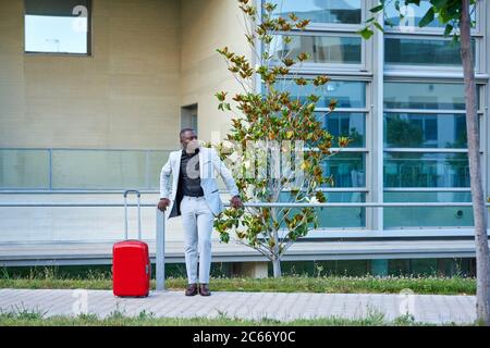 African-American in a white suit and a red suitcase. Businessman. Businessman traveling on business. Traveling man. Stock Photo