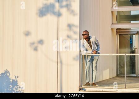 African American businessman at sunset in a building. He is basking in the evening sun. The shadow of a tree is projected on the wall Stock Photo