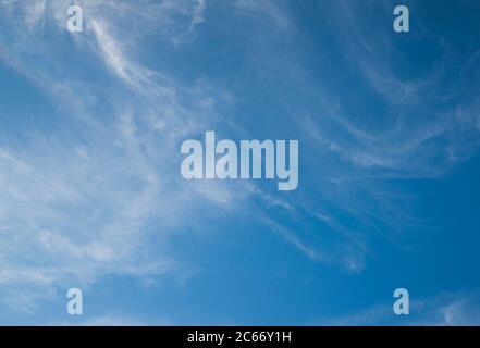 Fast moving clouds during a sunny day in the blue sky with the transition to evening hours along with the occasional flight of the aircraft leaving wh Stock Photo