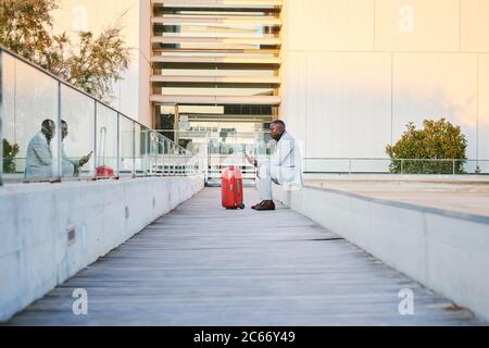 Traveler with a red suitcase and a cell phone. She's African-American and wears a fancy suit. Stock Photo