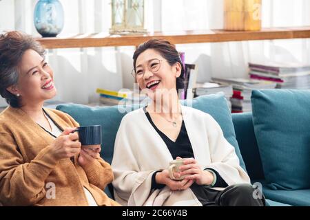 Happy old sisters sitting on the sofa catch up a cup of tea Stock Photo
