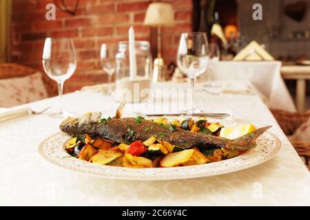 Grilled sea bass with vegetables on restaurant table, toned Stock Photo