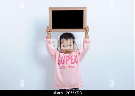 Cut asian girl holding blank chalkboard or blackboard. You can text it back to school isolated on grey background Stock Photo