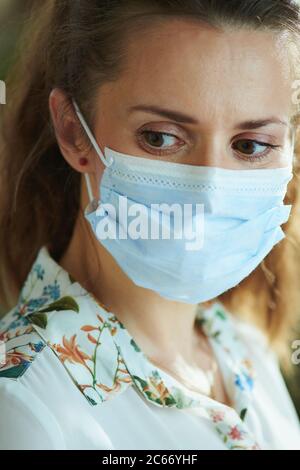 Life during coronavirus pandemic. pensive modern 40 years old woman in white blouse with medical mask. Stock Photo