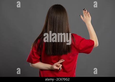 Long haired graduate nurse faking an oath with her back to the camera on a gray background Stock Photo