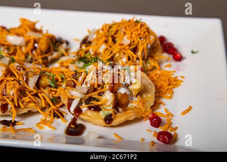 Crispy wheat biscuit topped with chickpeas, sprinkled with fine noodles, yogurt sauce, mint and tamarind Stock Photo