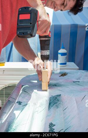 Man using a drill to build a piece of furniture on a rooftop. Stock Photo