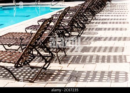 Swimming pool deck lounge chairs lined up by the side of a pool. Stock Photo