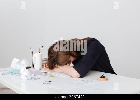 Photo of tired lady sitting at the white desk and sleeping while leaning head on her hands isolated Stock Photo