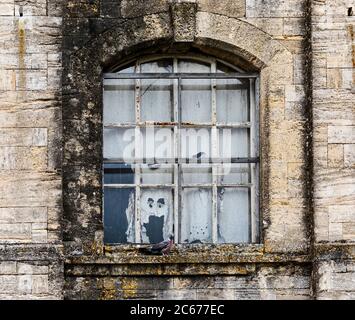 Torn curtain in derelict building window looking like a ghost or The Scream Stock Photo