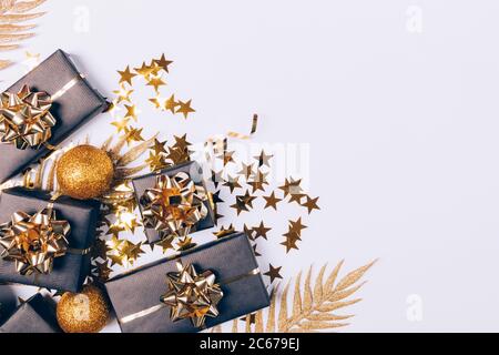 Christmas flat lay composition of shiny glitter balls, black gifts boxes with golden leaves and confetti on white background. Stock Photo