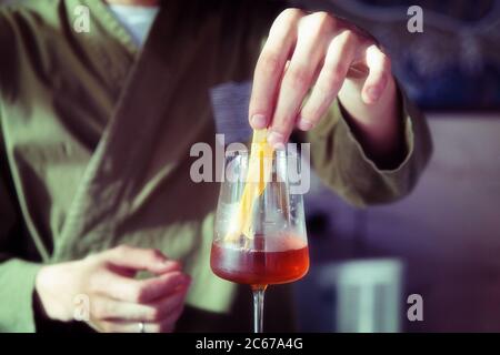 Male bartender is adding lemon zest to cocktail in wine glass, toned Stock Photo