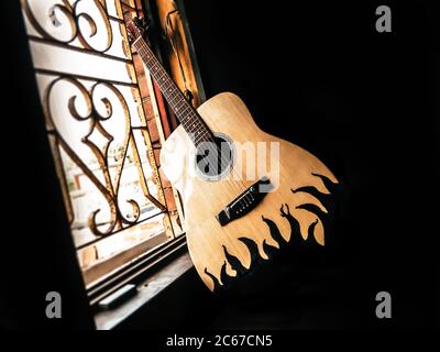An acoustic guitar placed next to the old vintage window with soft sunlight coming from. Nostalgia guitar chords. Summer melody background. Close up. Stock Photo