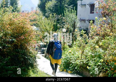 Rear View solo woman in hiking sportswear and with a backpack on her shoulders. Sporty woman with backpack walking outdoors. Travel girl stands on gar Stock Photo