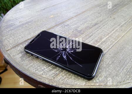 Viersen, Germany - July 6. 2020: Closeup of isolated mobile phone with cracked glass display on wood table Stock Photo