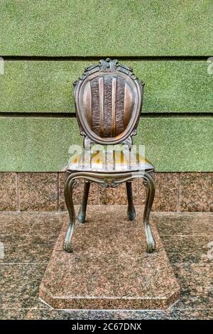 Bronze chair monument on a marble pedestal against the background at the green wall Stock Photo