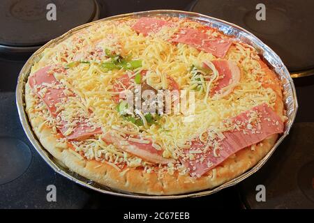 Frozen special pizza in an aluminum tray on a cooktop ready to bake in the oven. Shallow depth of field Stock Photo