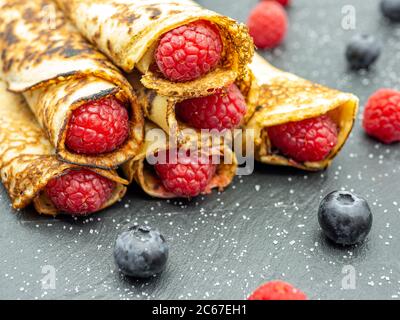 Crepes filled with jam and fresh raspberry and blueberries on black slate Stock Photo