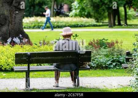 An old woman rests in a park bench on a sunny summer day Stock Photo
