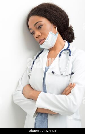Portrait of an African American tired female doctor in white coat. A sad nurse in a mask stands near the wall of the clinic. Stock Photo