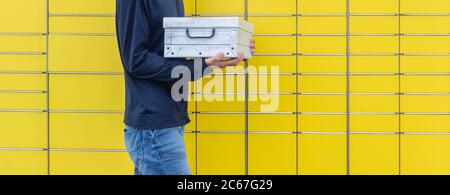 Parcel holding in hands and sending using yellow self-service post terminal machine. Hands with shipment to send using locker. Client holds received p Stock Photo