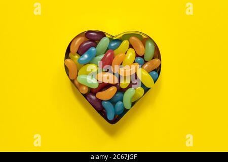 Multi-colored glazed jelly beans sweets in heart cookies mold on yellow background with copy space Stock Photo