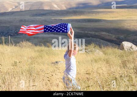 American flag. Little patriotic happy girl running with american flag waving on nature outdoor background. USA celebrate 4th of July. Stock Photo