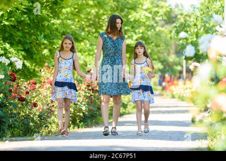 young woman walks down the path in the flowering garden by the hand with her two daughters Stock Photo