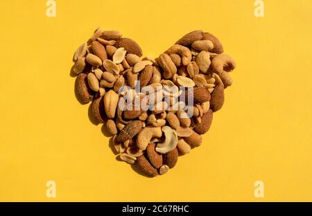 Various nuts in a heart shape on yellow background. Top view. Different kind of tasty and healthy nuts, snack. Stock Photo