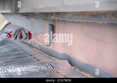 Man painting home socle with paint roller. Close up of rolling grey paint on building plinth. Home renovation Stock Photo