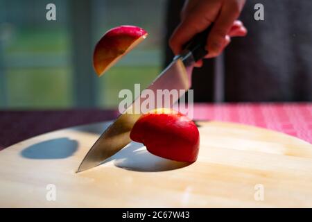Close up of chef hand chopping apple in half with kitchen knife on the table. Slicing red apple on wooden board Stock Photo