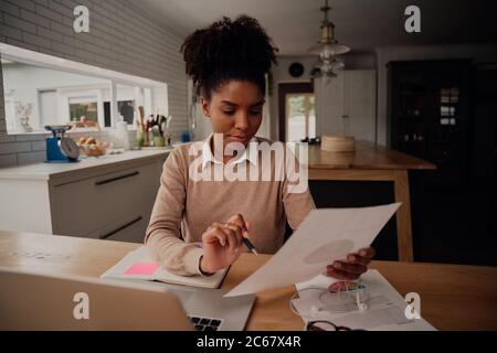 Young female freelancer analysing documents and comparing growth while working on laptop at home during covid-19 lockdown Stock Photo