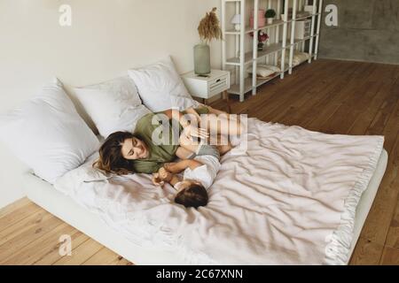 Happy mother playing with her little boy on bed. Stock Photo