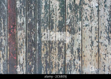 Detail of a wooden wall of a barn made of vertical, weathered boards with peeling green and red paint Stock Photo