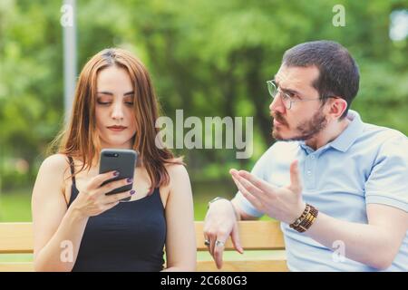 An arguing couple view, man is dictating, woman stay cool and unconcerned whie looking mobile phone Stock Photo