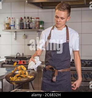 young chef prepares potatoes in a pan. Reversed by ejection Stock Photo
