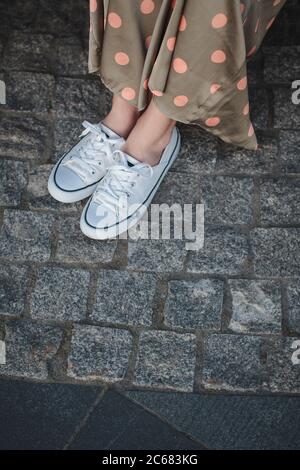 Female legs in white sneakers on the background of paving stones Stock Photo