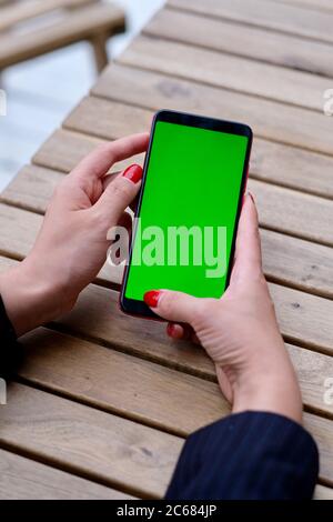 first person view of business woman using green screen smartphone. Blur wooden table background Stock Photo