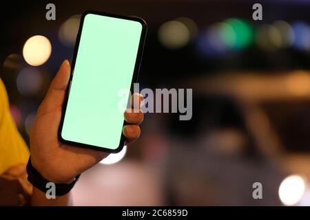 close up one person showing green screen smartphone at night. Blurred car and colorful traffic lights background Stock Photo
