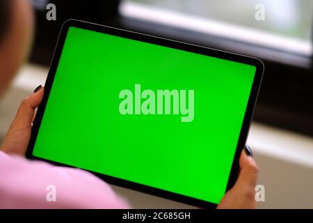 Over shoulder of woman holding green screen tablet device near window. Blur background Stock Photo