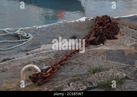 Rusty chain lying on the dockside with water in background  Stock Photo