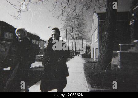 Fine 70s vintage black and white lifestyle photography of two women walking on the street dressed in their winter coats. Stock Photo