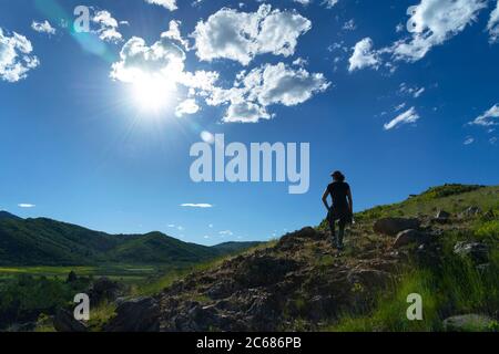 Woman hiker on mountain summit with sun flare looking down at valley below, Utah USA Stock Photo