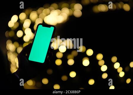 close up one hand holding green screen phone in darkness. Golden bokeh background Stock Photo