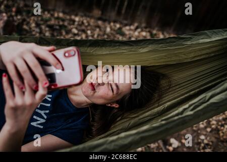 Teen girl laying in hammock making silly faces into phone Stock Photo