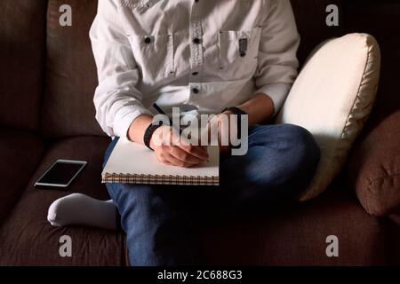 Close-up of a young man writing in a notebook sitting on a couch Stock Photo