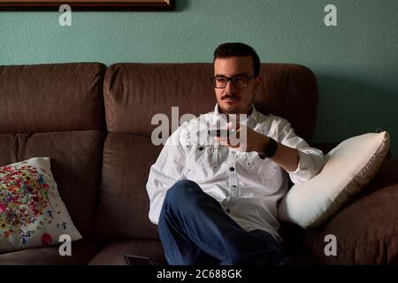 Young man changes channels with his remote control at home Stock Photo