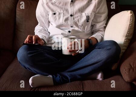 Close-up of a young man looking at his smartphone sitting on a couch Stock Photo