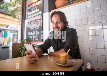 Young man laughing while looking at the mobile phone and drinking coffee Stock Photo