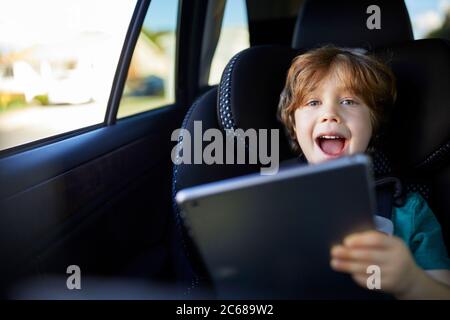 Portrait of happy boy using tablet PC while sitting at back seat in car Stock Photo